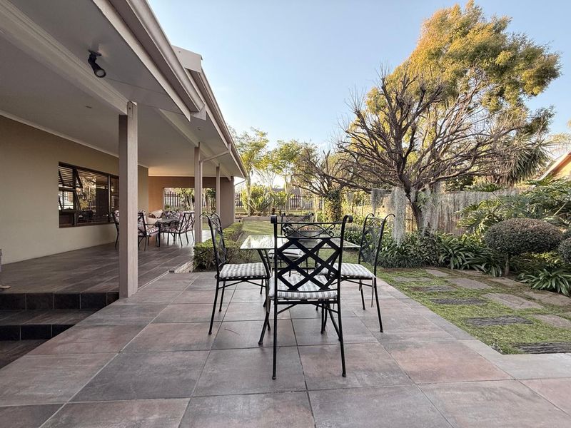 A spacious covered patio featuring tiled flooring and recessed lighting, overlooking a well-maintained garden area.