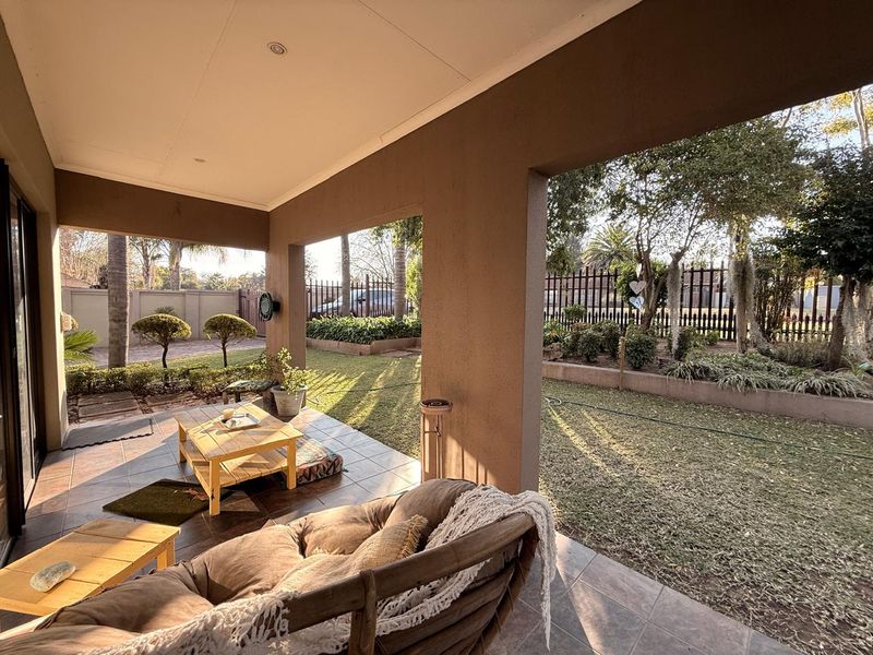 A covered outdoor patio area featuring tiled flooring and recessed lighting, overlooking a landscaped garden with established trees and perimeter fencing.