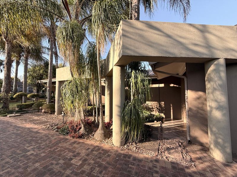 A well-maintained front entrance featuring a paved driveway, structural concrete pillars, and established garden landscaping.