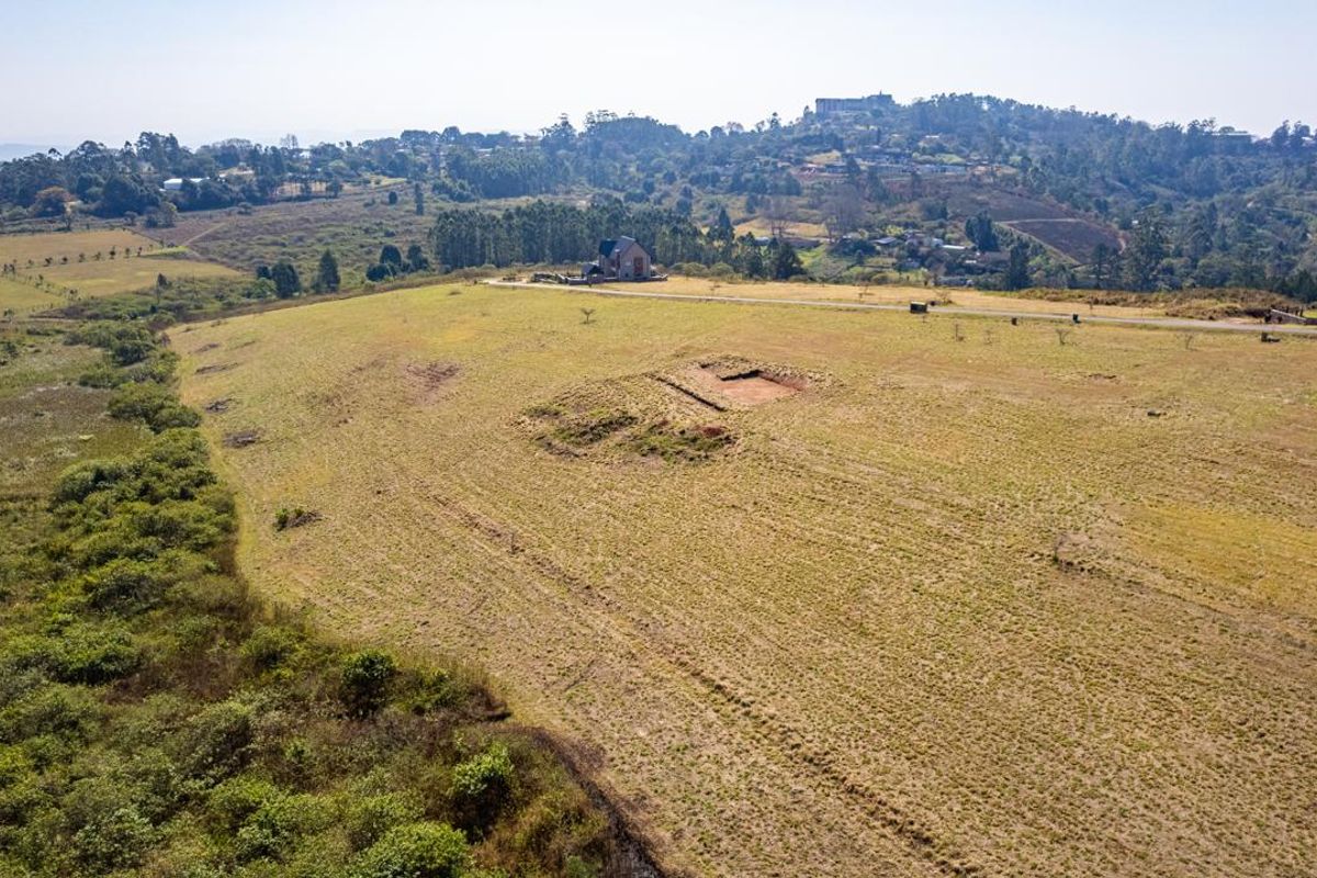 An aerial view of a large, open vacant residential plot featuring natural grassland and a small excavated area.