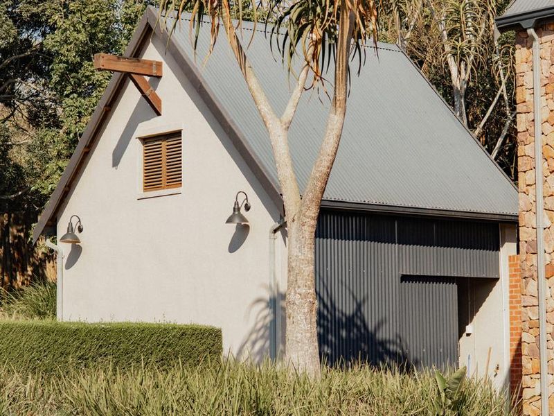 A well-maintained residential structure featuring a pitched corrugated metal roof, timber accents, and modern gooseneck lighting, set within a landscaped garden.