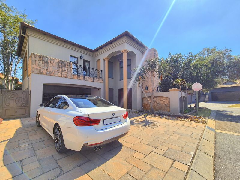 Front elevation of a double-story house featuring stone cladding, a paved driveway, and a covered entrance with architectural columns.