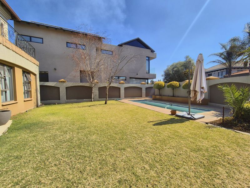 Rear garden featuring a well-maintained lawn, a swimming pool with paved surround, and high boundary walls providing privacy.