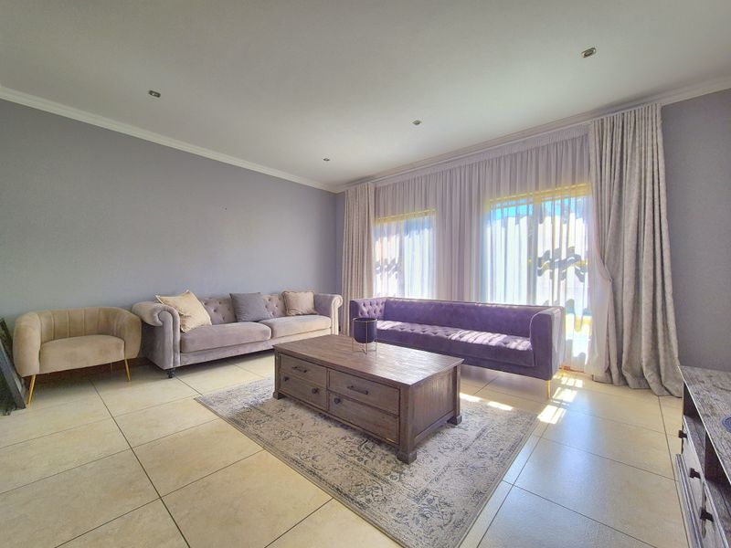 A bright and spacious living room featuring large sliding glass doors, neutral tiled flooring, and recessed downlighting.