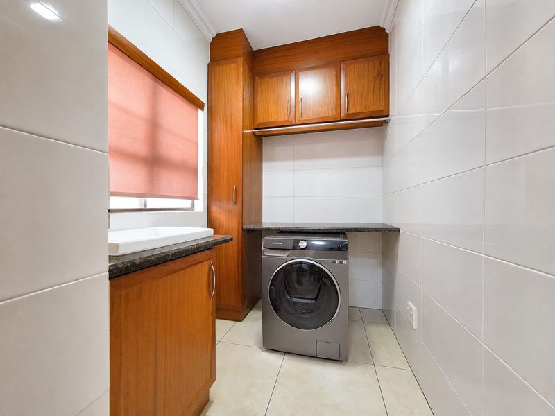 A functional laundry room featuring built-in wooden cabinetry, granite countertops, a sink, and tiled finishes throughout.