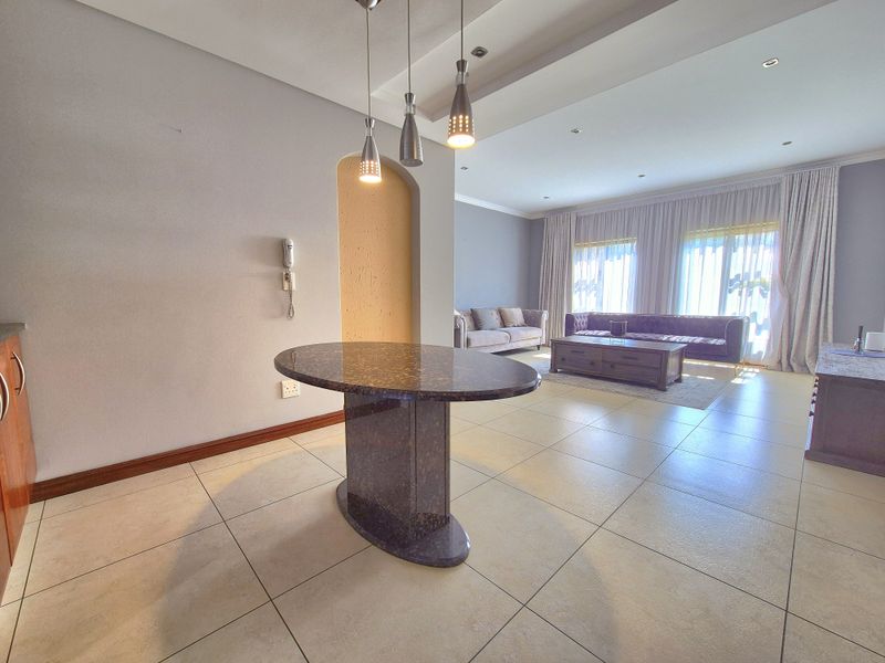 Spacious open-plan living area featuring tiled flooring, a central stone breakfast bar, recessed ceiling lighting, and an arched feature wall.