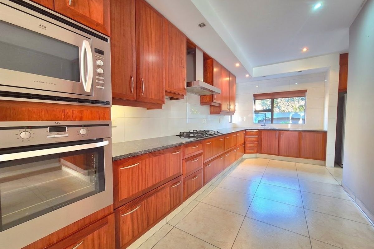 A spacious, well-maintained kitchen featuring warm-toned wooden cabinetry, granite countertops, built-in appliances, and large floor tiles, offering a clean and functional workspace.