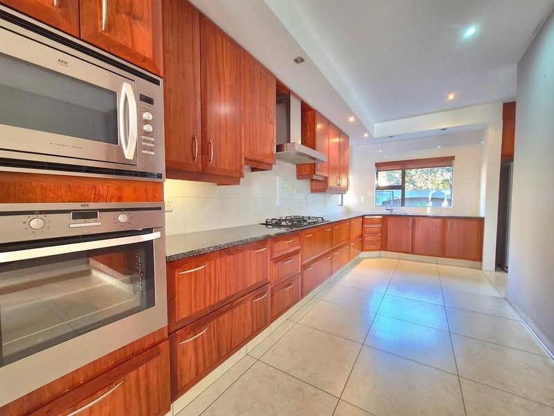 A spacious, well-maintained kitchen featuring warm-toned wooden cabinetry, granite countertops, built-in appliances, and large floor tiles, offering a clean and functional workspace.