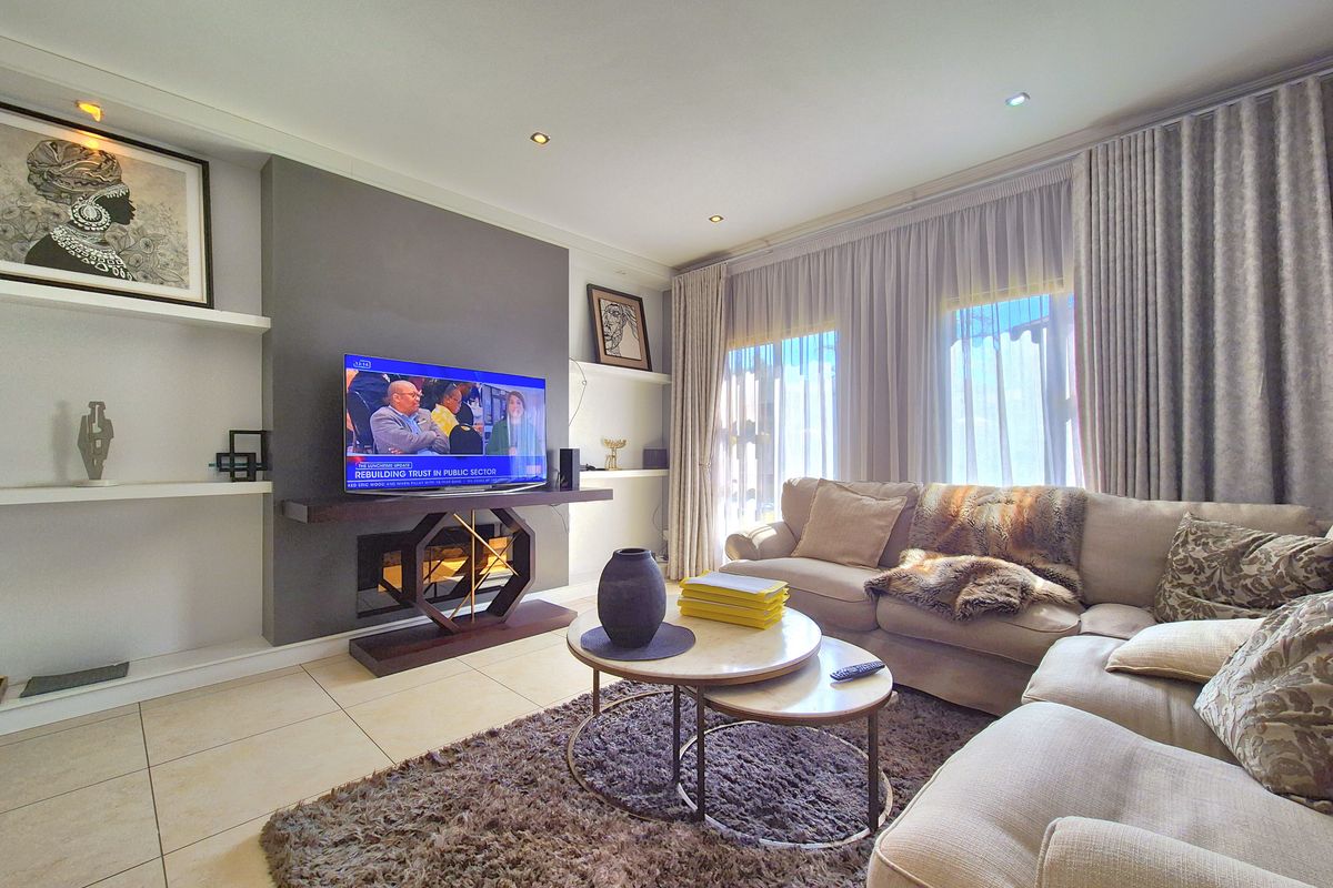 A well-maintained living room featuring a modern feature wall, built-in shelving, recessed downlighting, and large windows with floor-to-ceiling curtains.