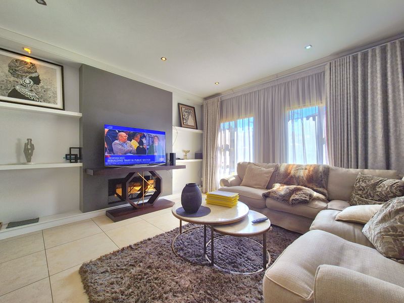 A well-maintained living room featuring a modern feature wall, built-in shelving, recessed downlighting, and large windows with floor-to-ceiling curtains.
