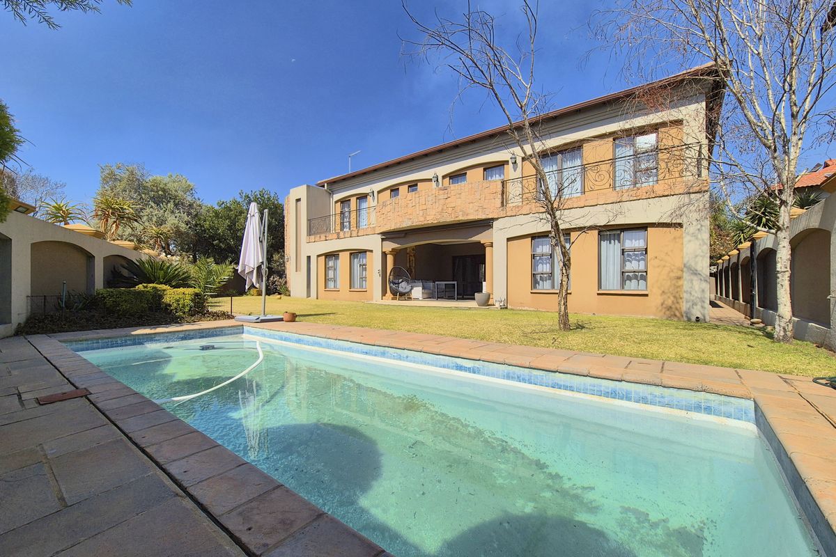 Rear view of a two-story house featuring a swimming pool, a lawn area, and an upper-level balcony with wrought iron railings.