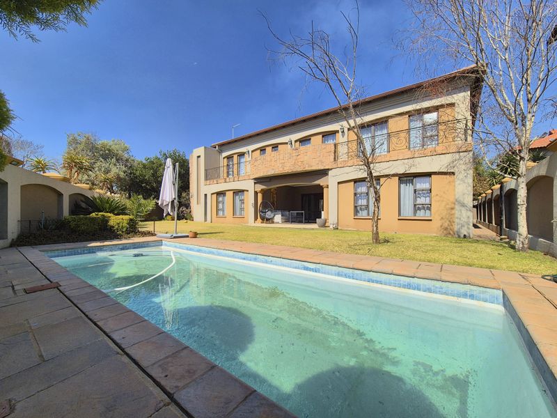 Rear view of a two-story house featuring a swimming pool, a lawn area, and an upper-level balcony with wrought iron railings.