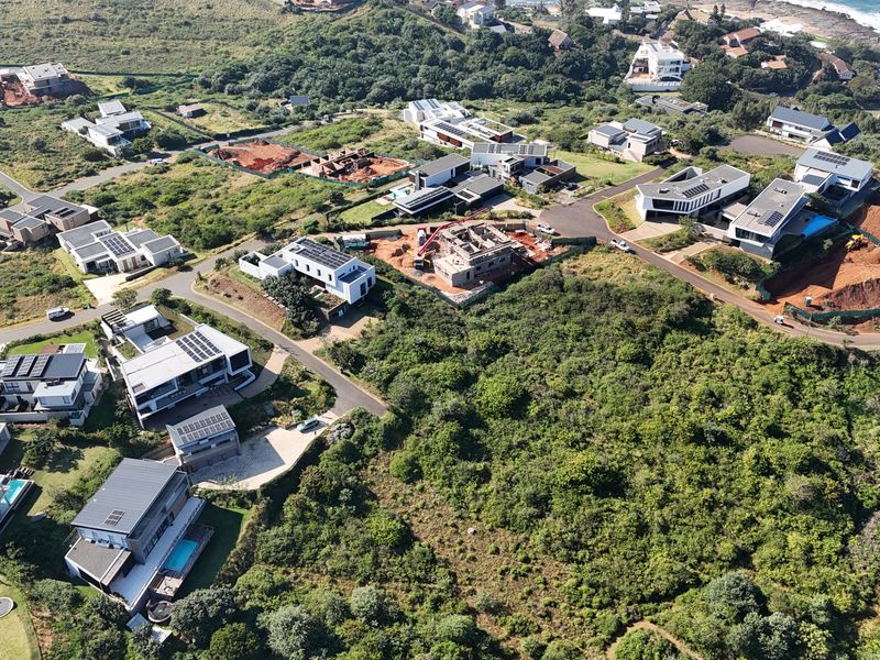 Aerial view of a coastal residential estate featuring modern homes, paved infrastructure, and surrounding natural vegetation near the coastline.