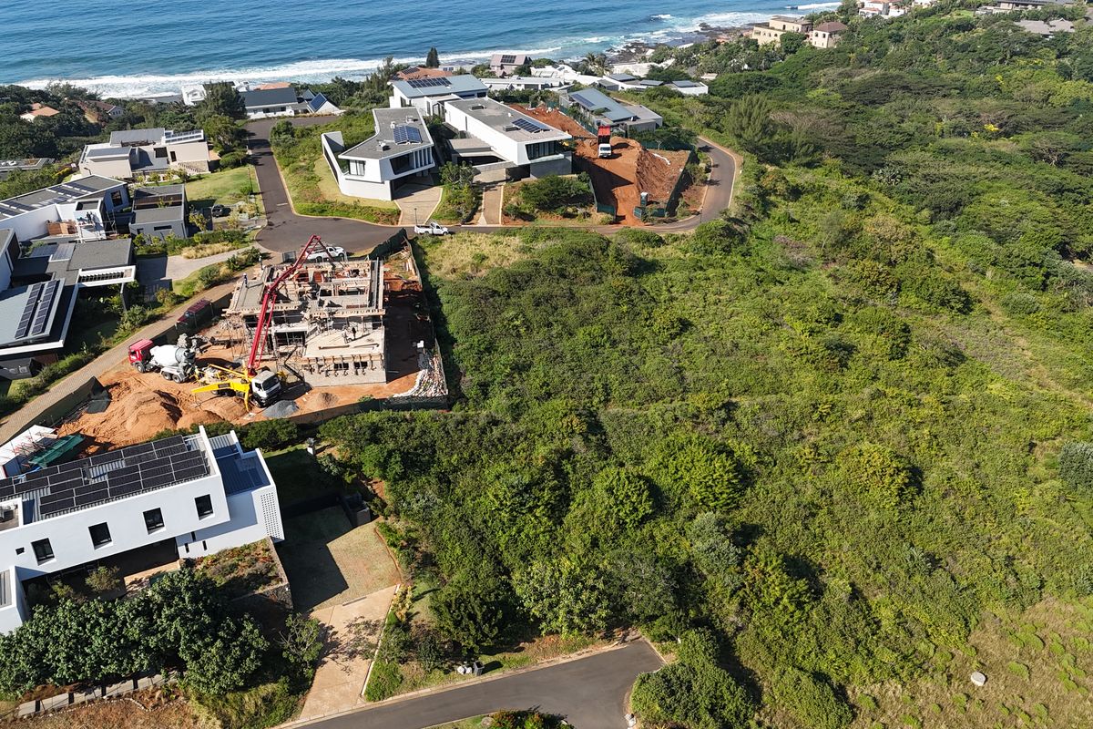 Aerial view of a vacant residential plot situated in a coastal estate, surrounded by established homes and natural vegetation.