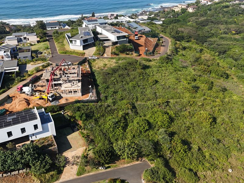 Aerial view of a vacant residential plot situated in a coastal estate, surrounded by established homes and natural vegetation.