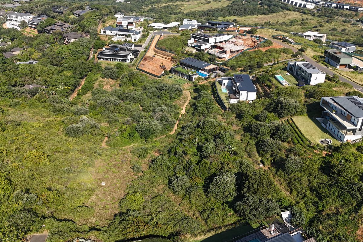 An aerial view of a vacant residential plot surrounded by established coastal vegetation and neighboring modern luxury homes.