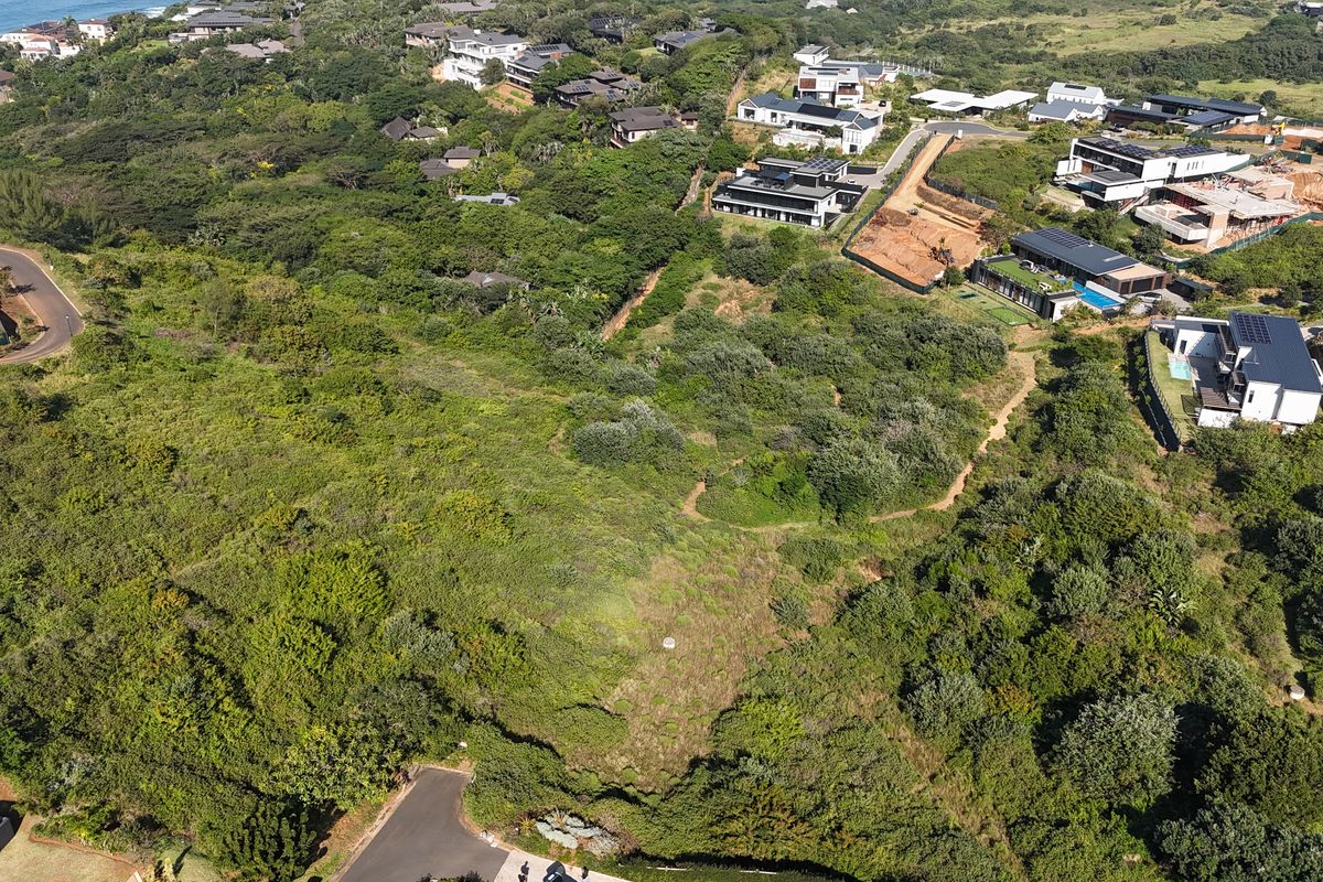 An aerial view of a vacant residential plot featuring dense natural vegetation and sloped terrain within an established coastal estate.