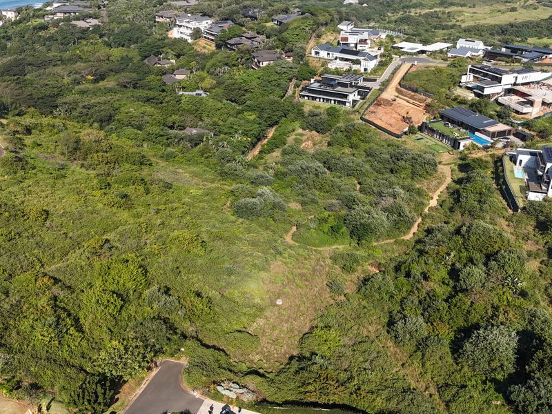 An aerial view of a vacant residential plot featuring dense natural vegetation and sloped terrain within an established coastal estate.