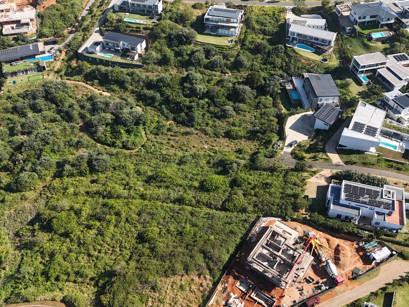 Aerial view of a vacant residential plot surrounded by established modern housing developments and natural vegetation.