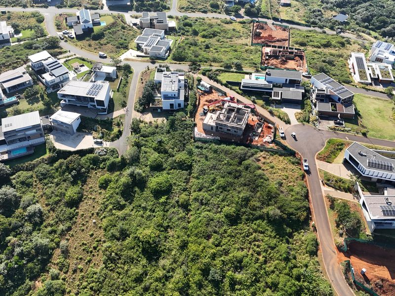An aerial view of a residential estate featuring modern homes, paved roads, and surrounding natural vegetation with ongoing construction projects.