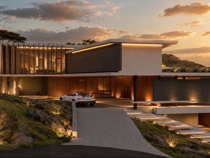 A modern luxury residence featuring stone cladding, cantilevered architecture, and integrated landscape lighting, set against a scenic hillside backdrop.