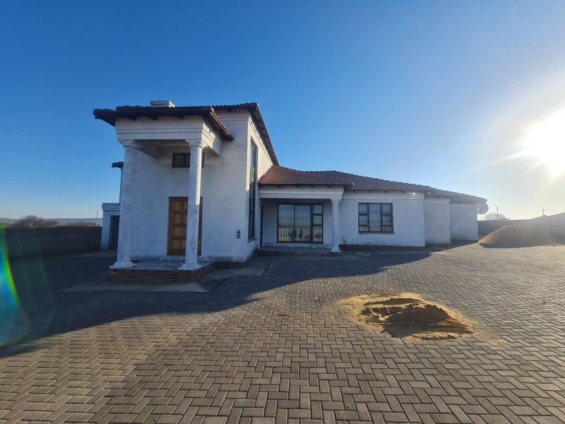 Front exterior view of a single-story house featuring a paved driveway, covered entrance porch with columns, and a tiled roof.
