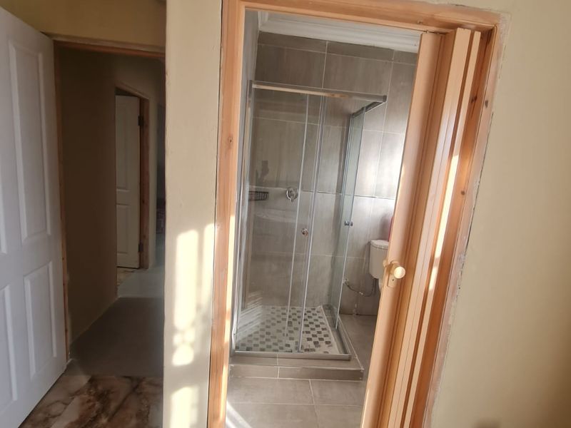 A bathroom featuring a glass shower enclosure and tiled finishes, currently showing unfinished door trim and requiring minor cosmetic completion.