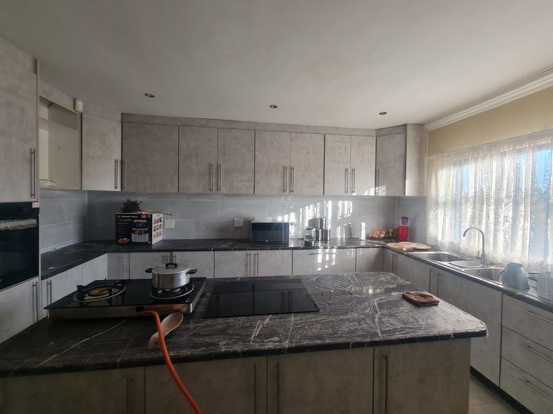 Modern kitchen featuring stone countertops, ample built-in cabinetry, a central island with a hob, and a double sink with natural light.