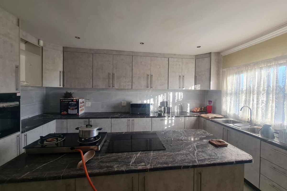 Modern kitchen featuring stone countertops, ample built-in cabinetry, a central island with a hob, and a double sink with natural light.