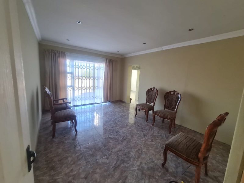 A spacious living area featuring tiled flooring, recessed downlighting, and a sliding glass door with a security gate leading to the exterior.