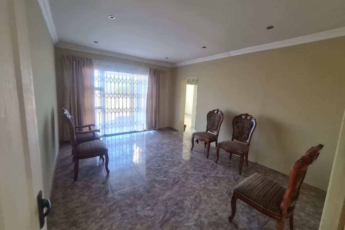 A spacious living area featuring tiled flooring, recessed downlighting, and a sliding glass door with a security gate leading to the exterior.