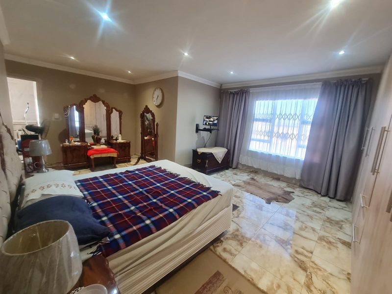 Spacious bedroom featuring tiled flooring, recessed downlighting, built-in cupboards, and a large window fitted with a security gate.