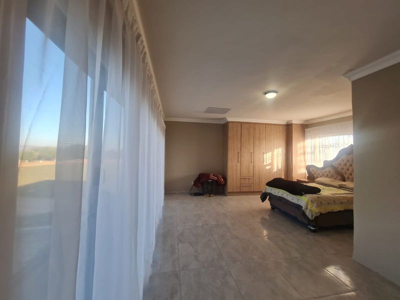 Spacious bedroom featuring large windows with natural light, tiled flooring, and extensive built-in cupboard storage.