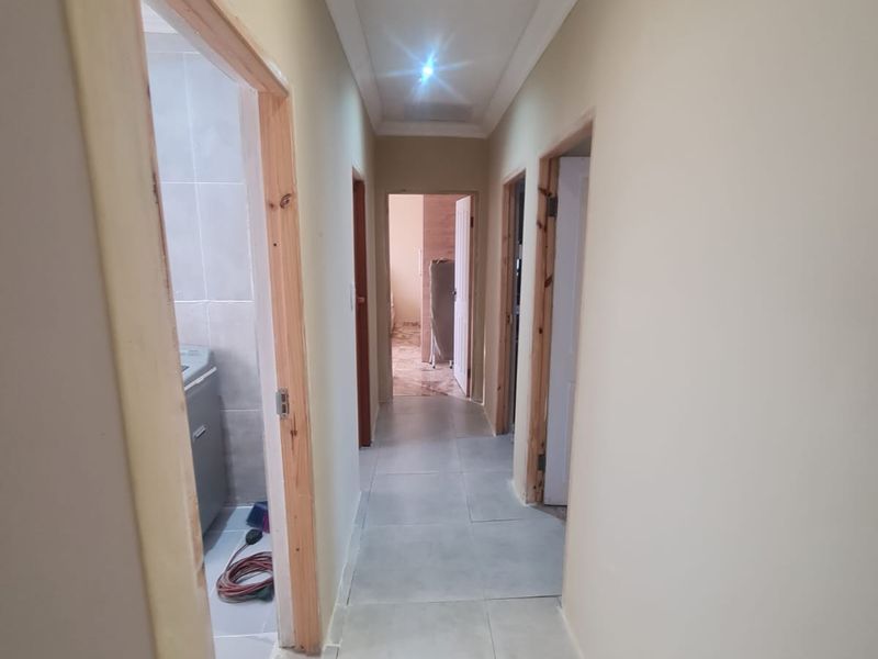 A bright, tiled hallway featuring recessed downlighting, cove cornicing, and unfinished timber door frames leading to adjacent rooms.