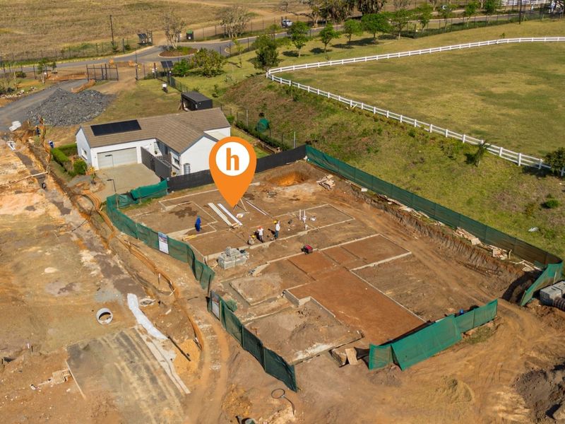 Aerial view of a residential construction site showing the concrete foundation slab and adjacent existing garage structure.