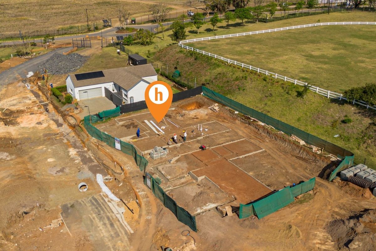 Aerial view of a residential construction site showing the concrete foundation slab and adjacent existing garage structure.