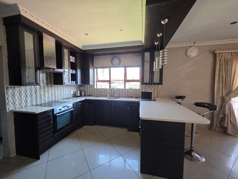 Modern kitchen featuring dark wood cabinetry, stone countertops, a breakfast bar, integrated appliances, and a mosaic tile backsplash with tiled flooring.
