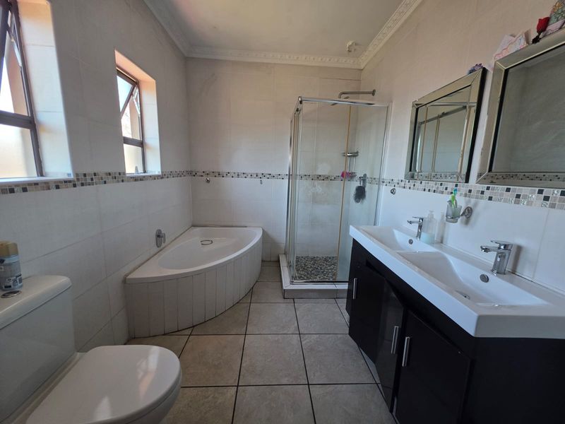 A spacious bathroom featuring a corner bathtub, a glass-enclosed shower, and a double vanity with modern fixtures and tiled finishes.