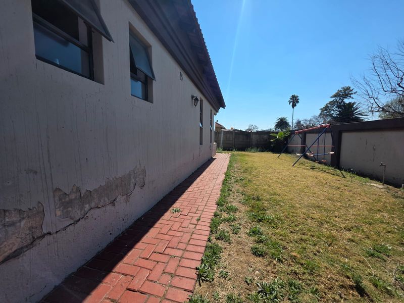 Rear exterior view of the property featuring a brick paved walkway, lawn area, and boundary wall, showing visible signs of exterior wall plaster damage.