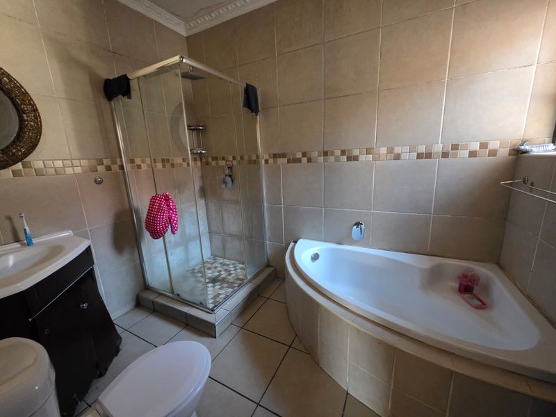 A functional bathroom featuring a corner bathtub, separate glass shower enclosure, tiled finishes, and a vanity unit with basin.