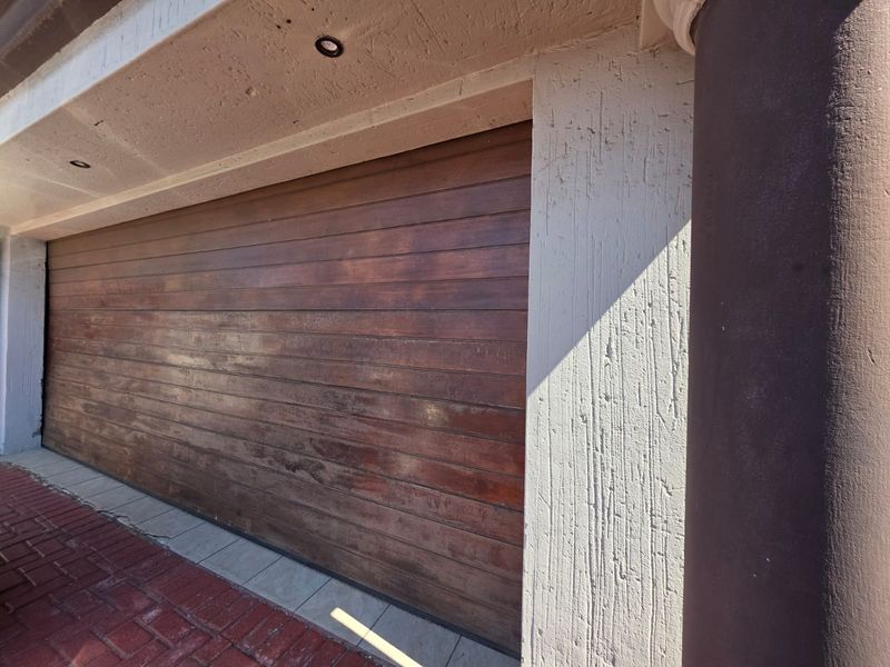 A close-up view of a wooden sectional garage door featuring a textured plaster facade and recessed lighting.