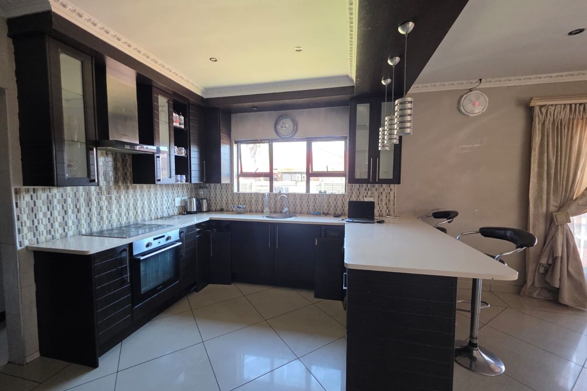 Modern kitchen featuring dark wood cabinetry, stone countertops, a breakfast bar, integrated appliances, and a mosaic tile backsplash with tiled flooring.