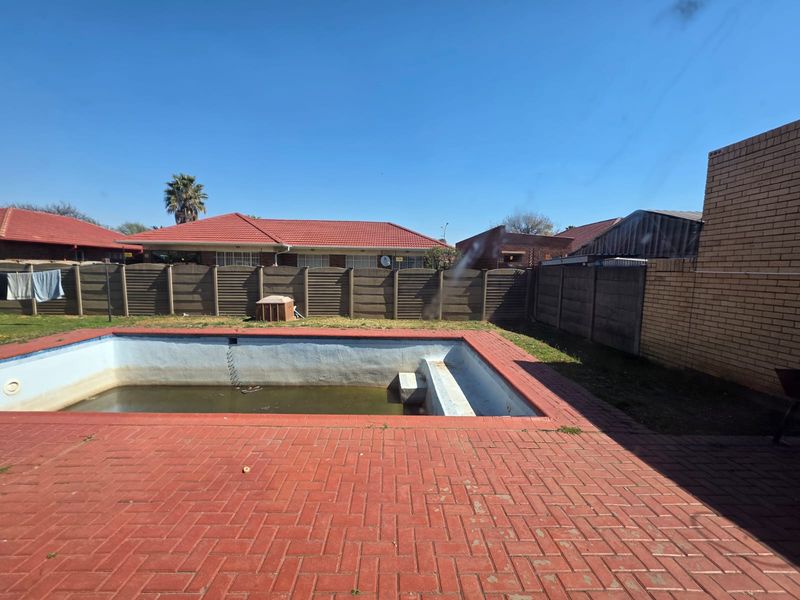 Outdoor pool area featuring a paved patio and a swimming pool requiring maintenance, enclosed by perimeter boundary walls.