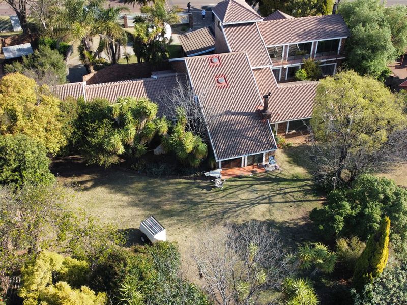 Aerial view of a large residential property featuring a multi-level tiled roof, chimney, skylights, and an expansive garden with a paved patio area.