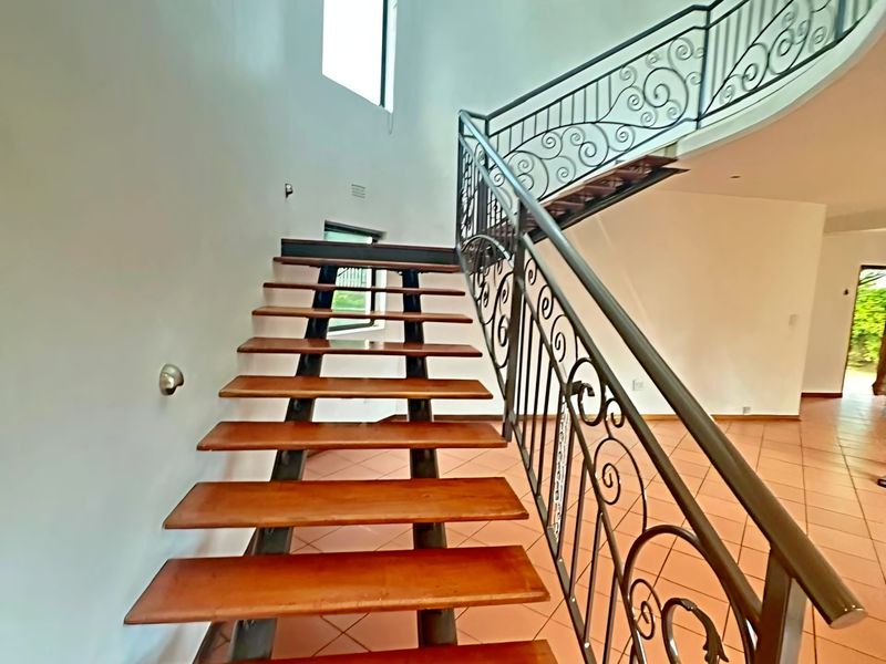 Spacious entrance hall featuring an open-tread staircase with decorative wrought iron balustrades and neutral tiled flooring.