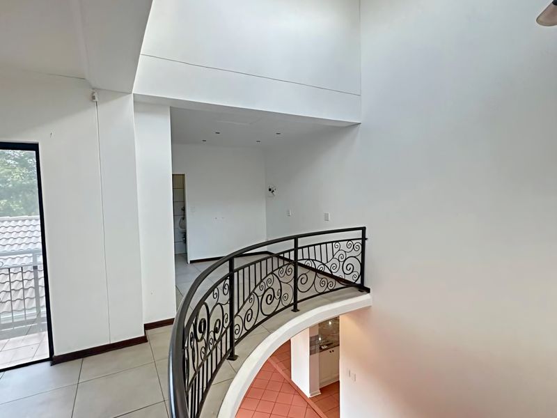 Spacious double-volume landing area featuring a decorative wrought iron balustrade, vaulted ceilings, and an arched window overlooking the staircase.