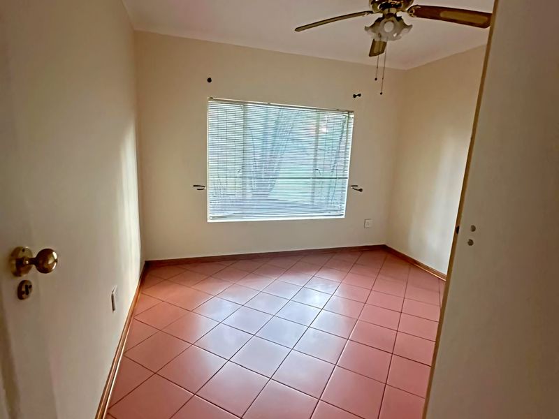 An empty bedroom featuring tiled flooring, a ceiling fan, and venetian blinds, ready for personalization.
