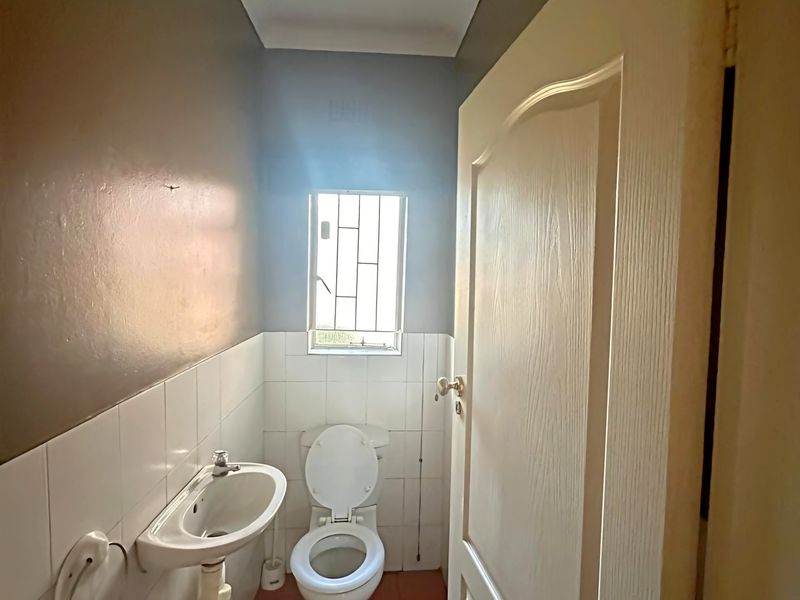 A compact guest bathroom featuring a pedestal basin, toilet, tiled walls and flooring, and a window with security bars.