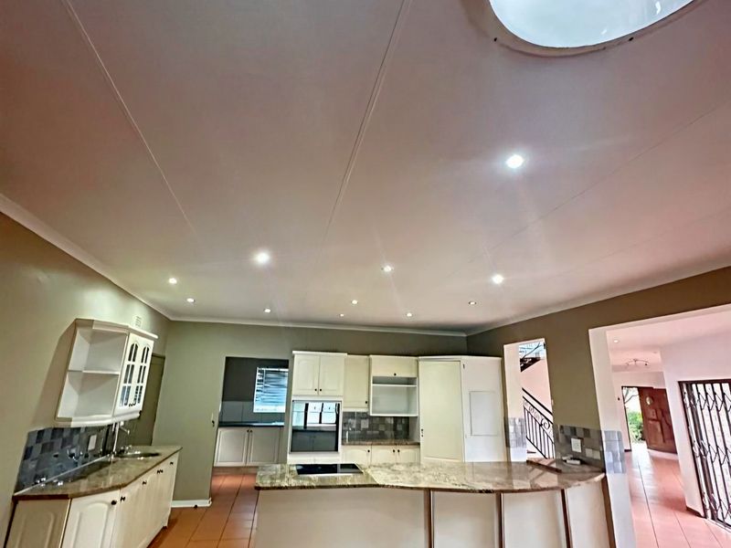 Spacious kitchen featuring built-in cabinetry, granite countertops, integrated oven, hob, and a large circular skylight, finished with tiled flooring.