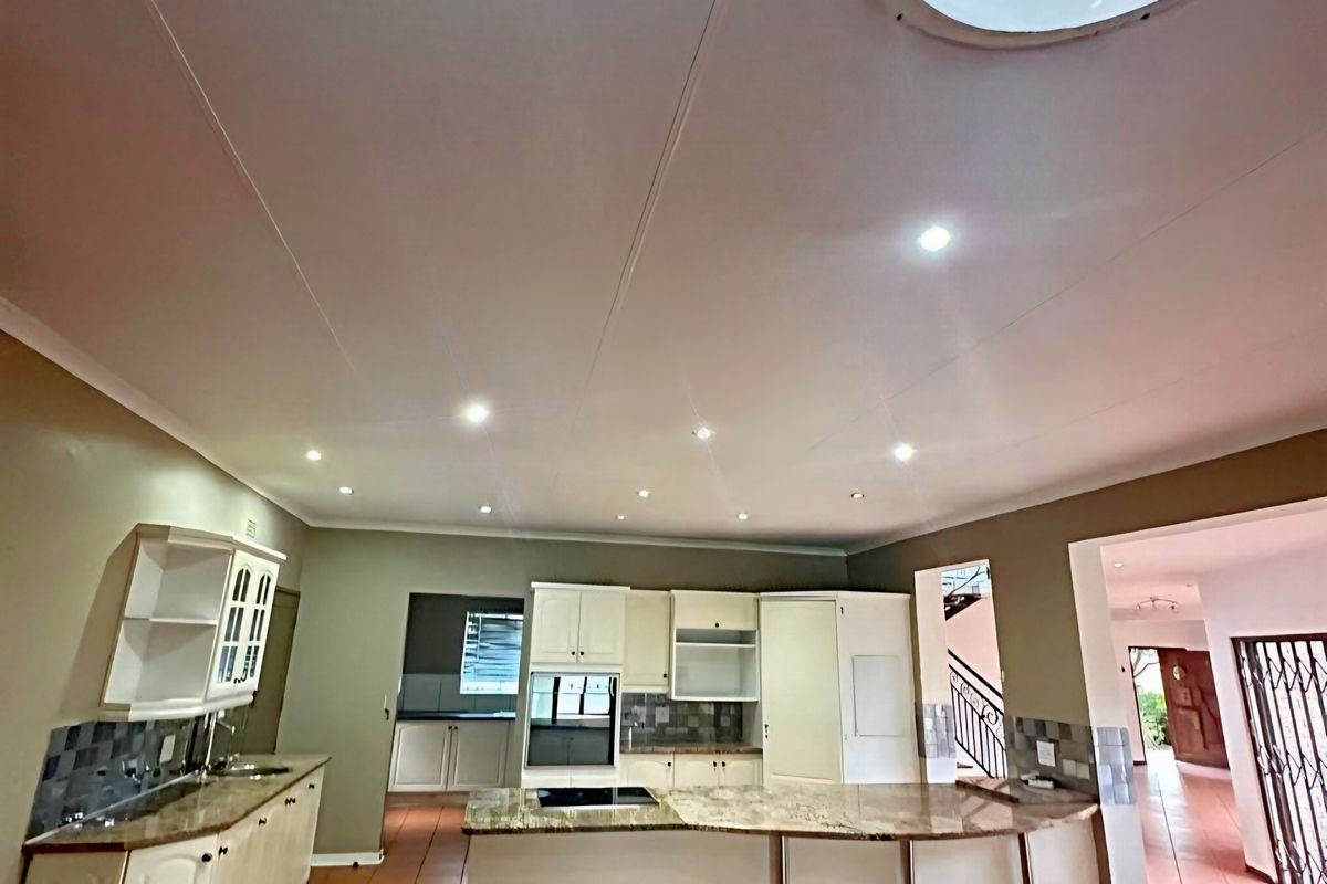 Spacious kitchen featuring built-in cabinetry, granite countertops, integrated oven, hob, and a large circular skylight, finished with tiled flooring.